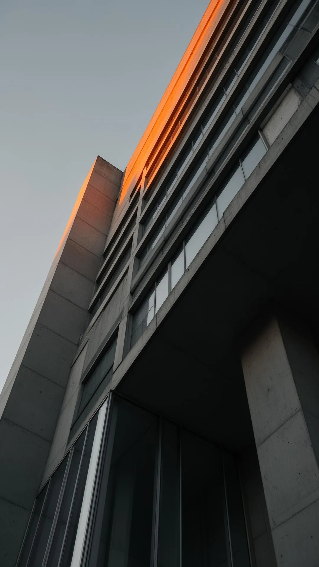 A modernist concrete and glass facade catching golden hour light — structure as the substrate of sustained impact.